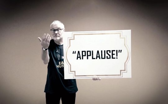 A person holding up a large sign that reads "applause!"
