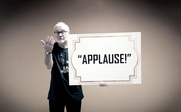A person holding up a large sign that reads "applause!"