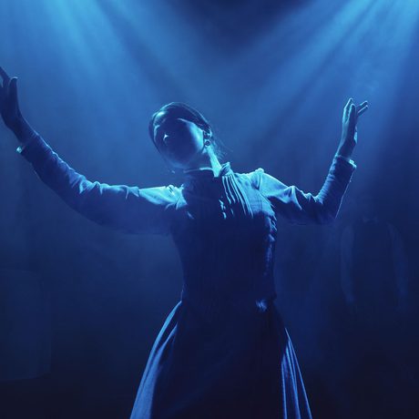A performer in a dress dancing under dim, blue lighting.