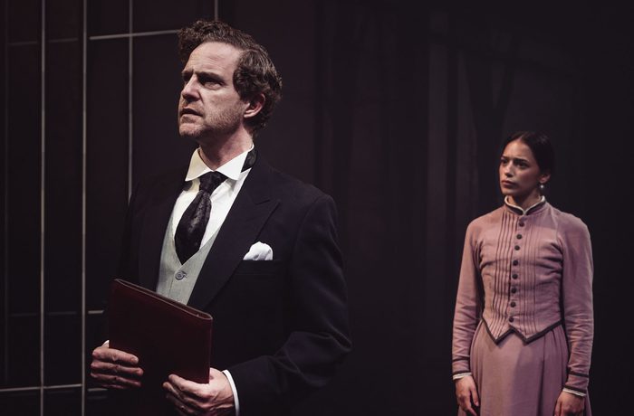 Two performers looking concerned, one holding a leather file.