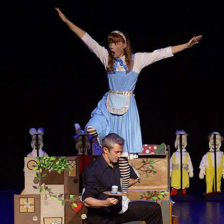 A performer as Alice standing on the shoulders of another performer.