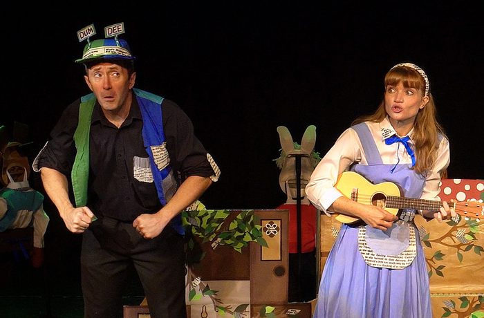 Two performers, once dressed as Tweedle Dee and Dum, and the other Alice, playing a guitar.