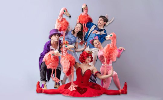 A group of people dresses as characters from Alice in Wonderland and holding pink flamingo puppets.
