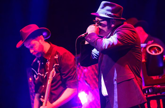 A persons playing a harmonica into a microphone, and a second person playing a guitar.