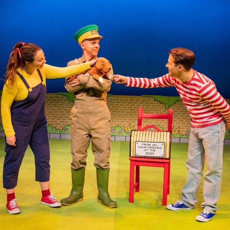 Three people standing together. One is dressed as a zoo keeper and holding a puppy dog puppet.