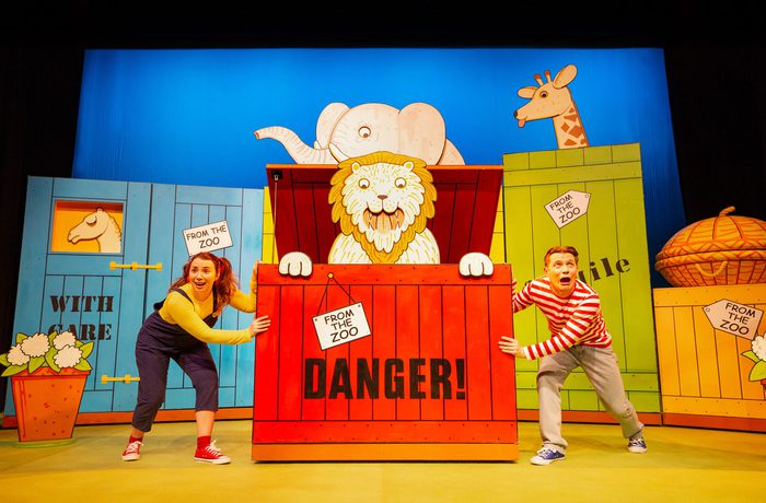 Two people surround by large cardboard props of animal crates.