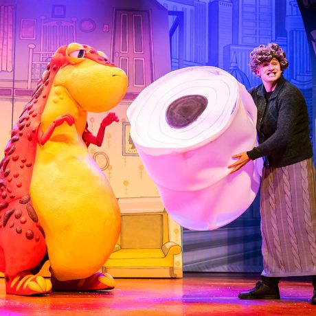 A person holding a giant toilet roll and a person in a large dinosaur costume.