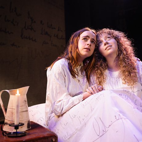 Two people in period night gowns, sitting down by a candle.