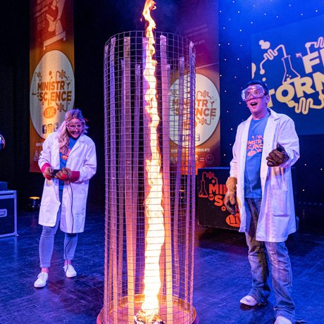Two people in lab coats looking at a large column of fire.