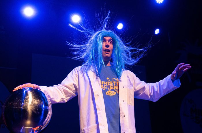 A person in a wig holding a metal ball, with their hair standing on end.
