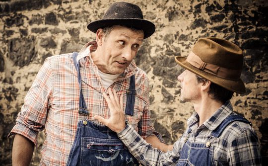 Two people dreesed as old farm hands wearing dungarees and hats