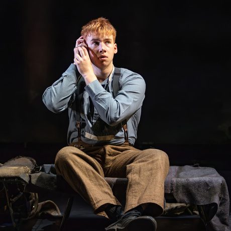 A performer sat on a bed with his hands to his head.