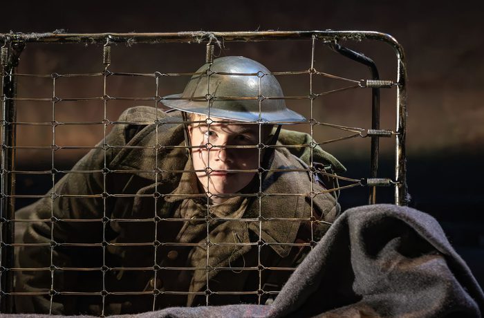 A performer dressed as a World War 2 soldier lying down behind a bed frame.