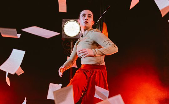 A person dancing in front of a spotlight, surrounded by falling sheets of paper.