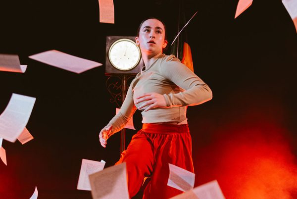 A person dancing in front of a spotlight, surrounded by falling sheets of paper.