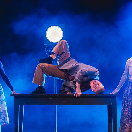 A person break dancing on a table with two people watching.
