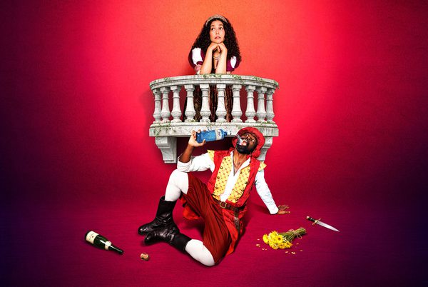 Two people in period costume. One is leaning on a balcony, the other is siting on the floor swigging from a bottle.