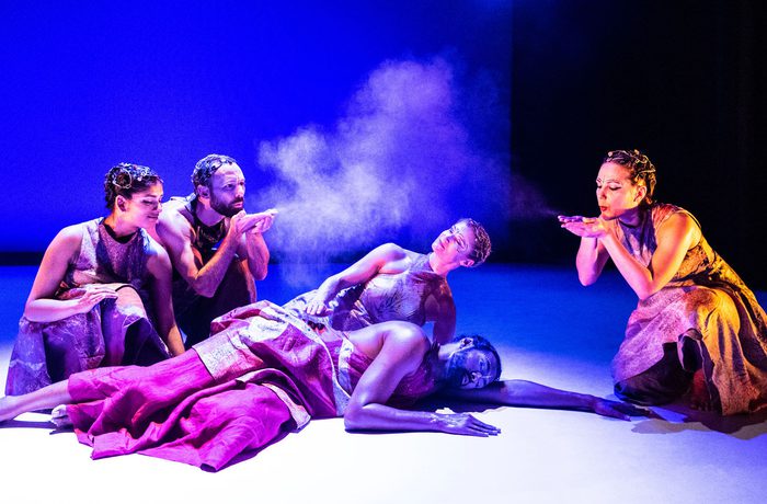Dancers lying on the floor, others crouched around blowing dust into the air.