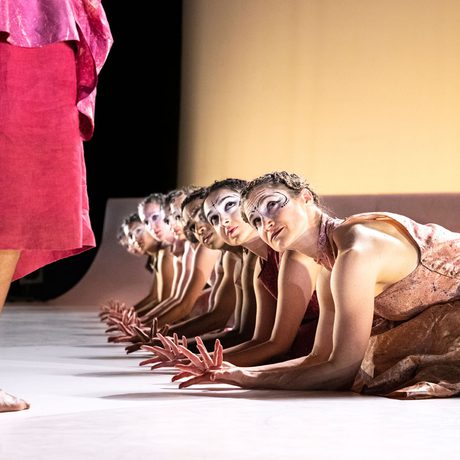 Dancers on their knees, bowing to someone pacing in front of them.