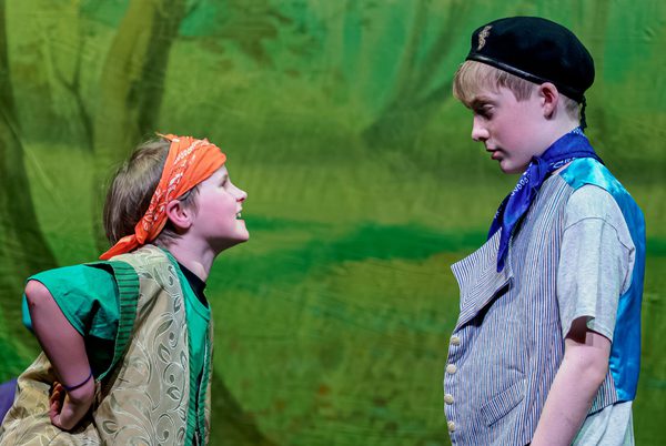 Two young people performing in front of a large green backdrop.