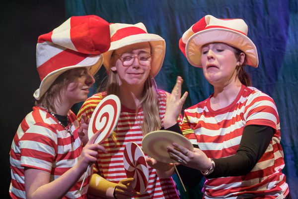 Three young people wearing matching stripy t-shirts and giant hats, and holding giant lollipop props.