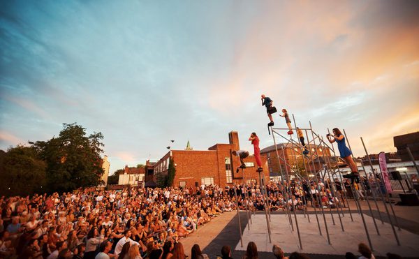 A large crowd outside watching acrobats perform on scaffold poles.