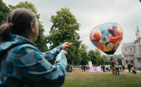 A person holding a rope to a hot air ballon.