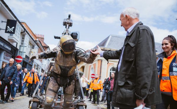 A person dressed as a space man holding hands with another person in the street.