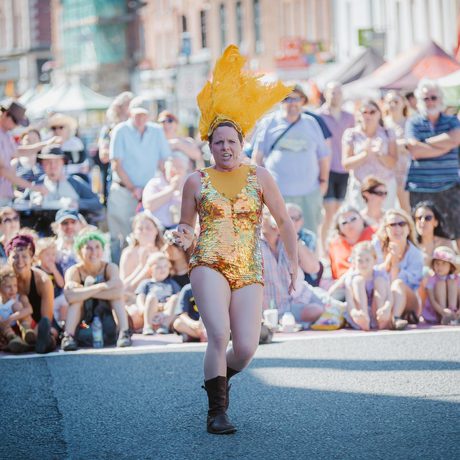 A person wearing sparkly gold outfit, performing to a large crowd outside.