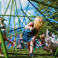 Young people crawling under large colourful poles in the grass.