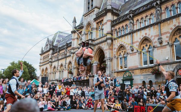 Acrobats performing with a large jumprope in front of a large crowd outside.