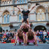 Acrobats performing a human pyramid. The person on top is doing a handstand.