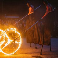 Two people on stilts pushing giant wheels on fire.