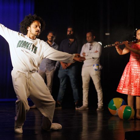 A person dancing on stage, to the music of another person playing the flute