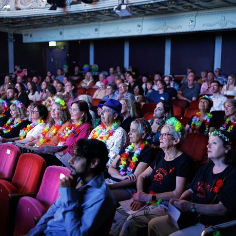 An audience sitting in a theatre auditorium, dressed in beach wear.