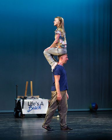 An acrobat standing up straight with another acrobat siting on their head