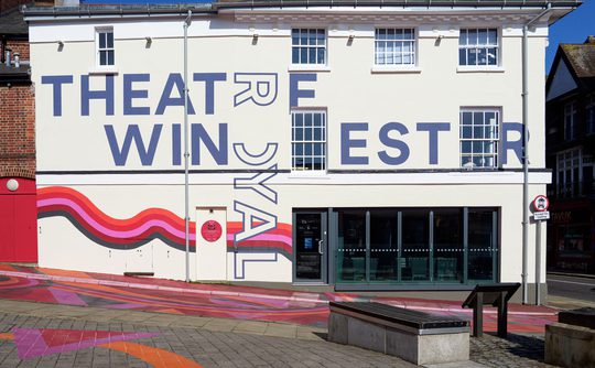 A daytime photo of Theatre Royal Winchester, with colourful artwork across the building and in the streets