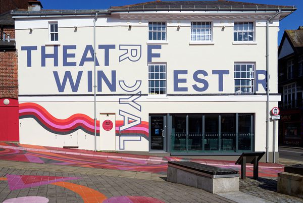 A daytime photo of Theatre Royal Winchester, with colourful artwork across the building and in the streets