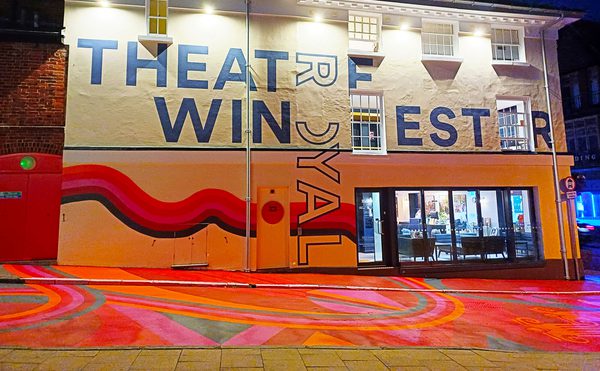 A nighttime photo of Theatre Royal Winchester, with colourful artwork across the building and in the streets