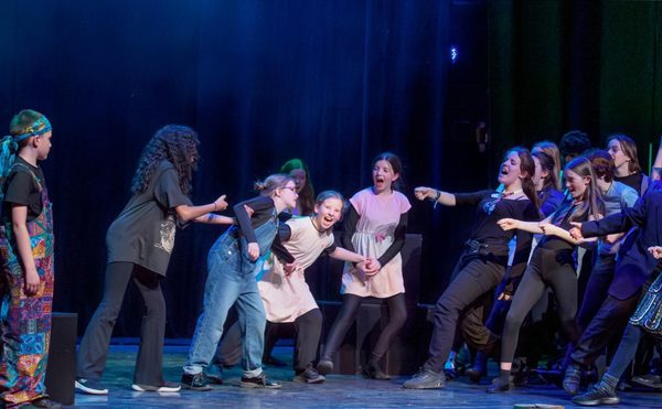 A group of young people on a stage, performing as part of a youth theatre