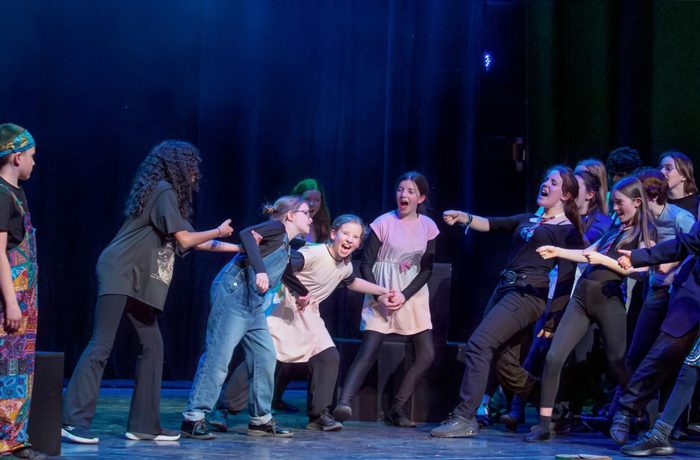 A group of young people on a stage, performing as part of a youth theatre