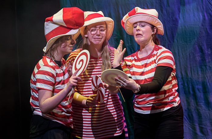 Three young performers on stage, dressed in red and white stripes and holding giant lolly props.