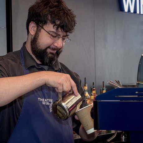 A person behind a bar pouring milk into a coffee.