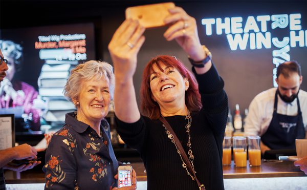 Two people stood into front of a bar, smiling and taking a selfie.