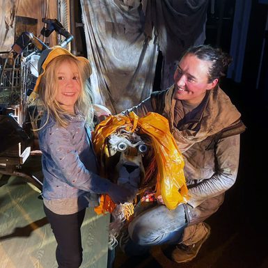 A young person and an adult on a theatre set holding a lion puppet.