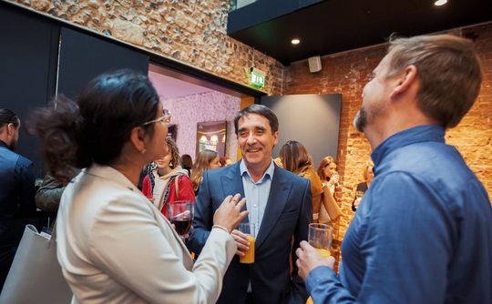 Three people dressed smarting with drinks and talking to each other.