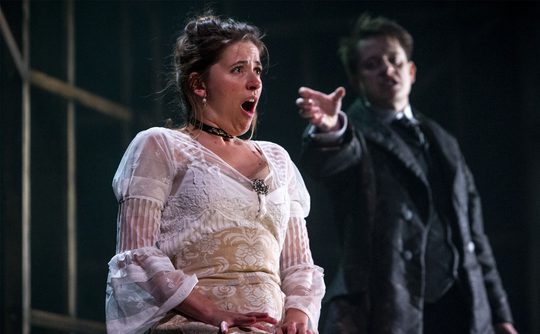 A person in a white dress sat looking horrified as a performer reaches for them from behind.
