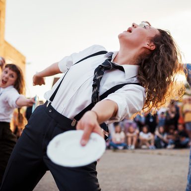 Performers dancing outdoors with white plates in their hands.