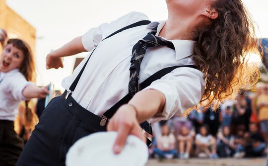 Performers dancing outdoors with white plates in their hands.