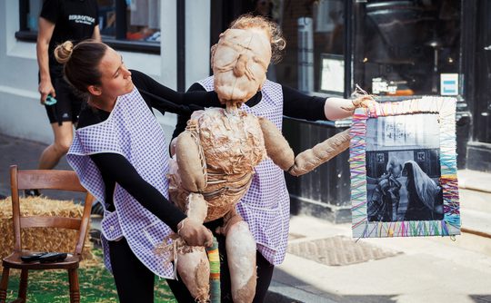 Two puppeteers operating a puppet outside.